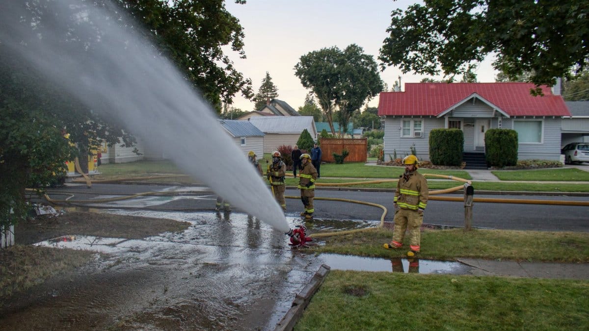 Firefighters operating a high-pressure hose in a residential neighborhood for emergency response.