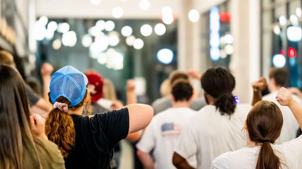 A diverse group of people raising their arms indoors with bright lighting.