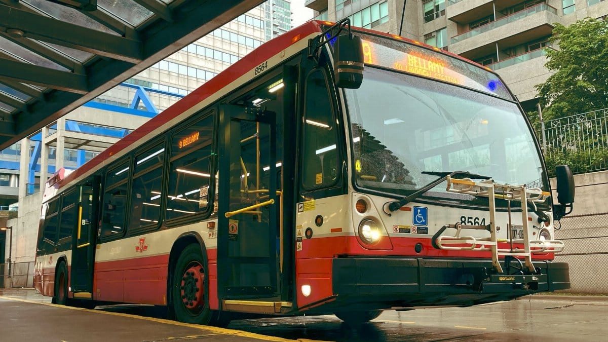 Toronto public transit bus parked at an urban terminal stop on a sunny day.