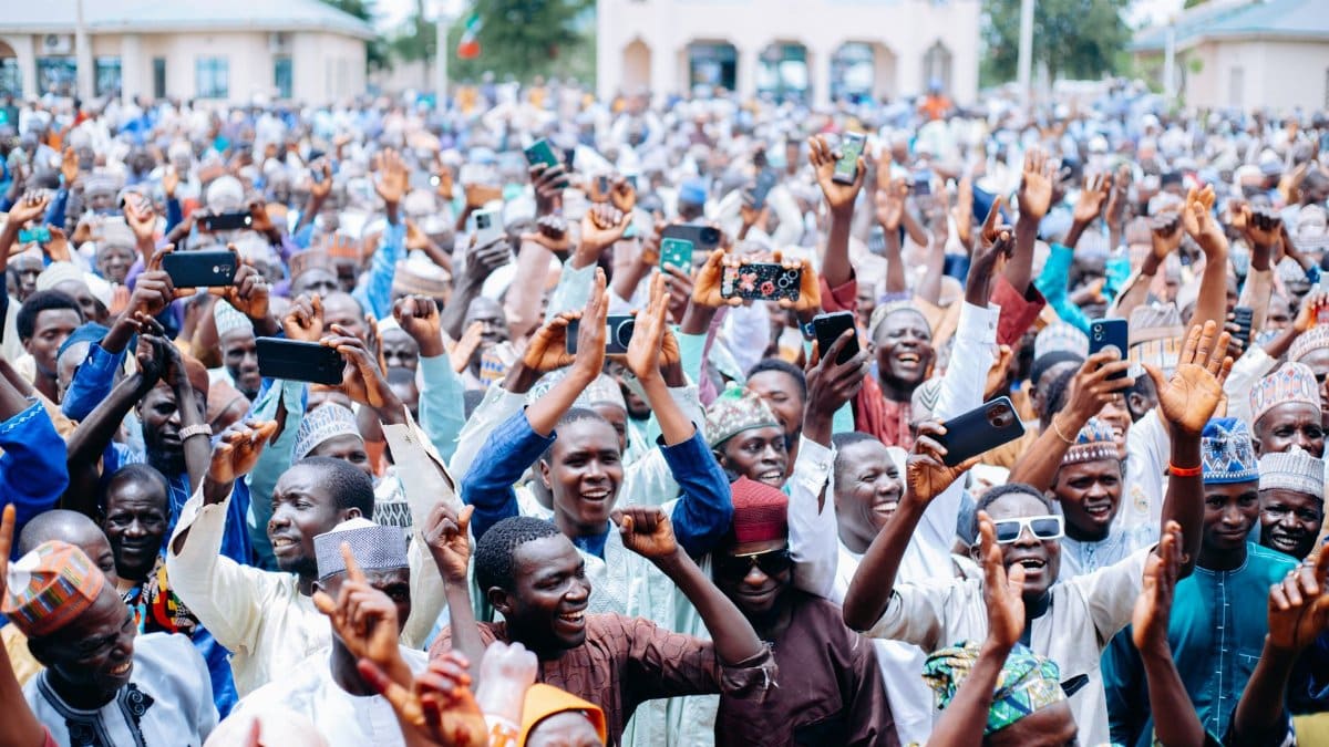 A large diverse crowd of adults celebrating outdoors with raised hands and smiles, capturing the joyful atmosphere.