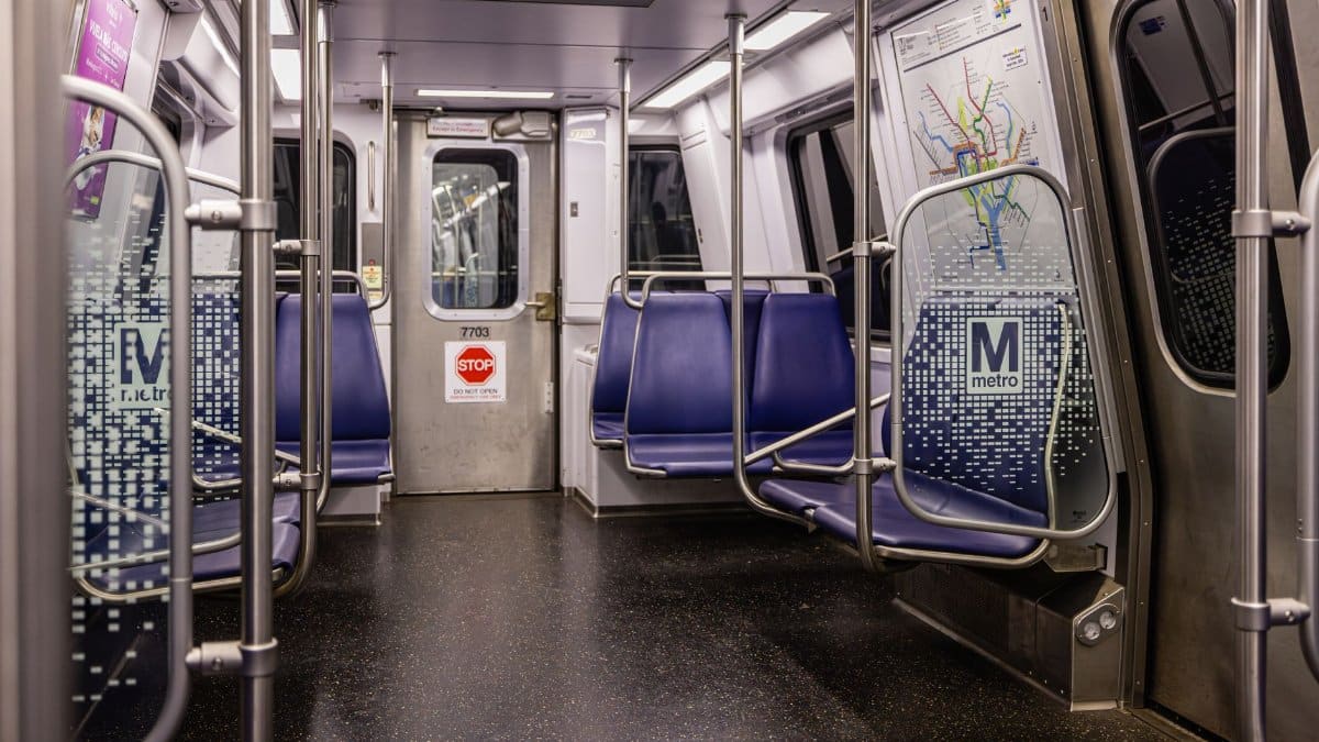 Interior view of an empty Washington DC Metro train car with blue seats and map display.