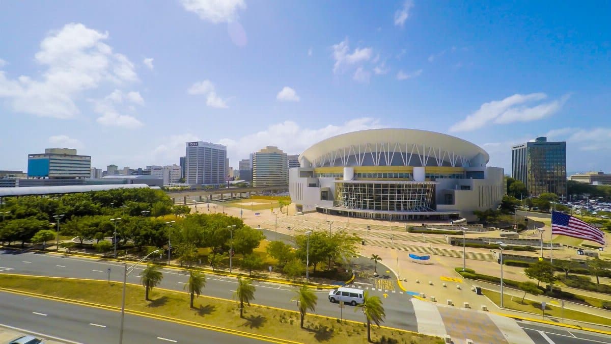 Aerial view of city district with contemporary buildings and indoor arena with green trees under cloudy sky on sunny day