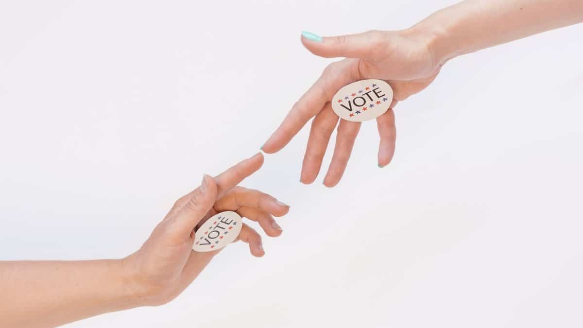 Two hands reaching with vote stickers, symbolizing participation and democracy in elections.