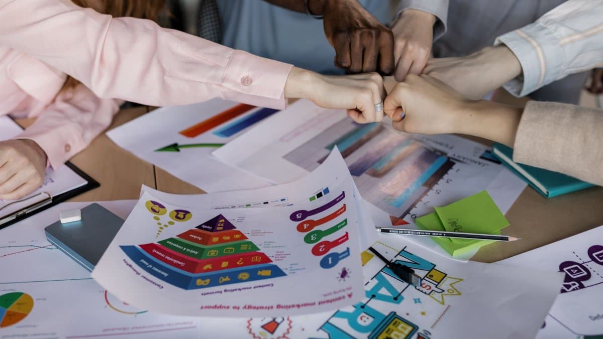 A diverse team unites hands over business reports and marketing strategies, symbolizing teamwork.