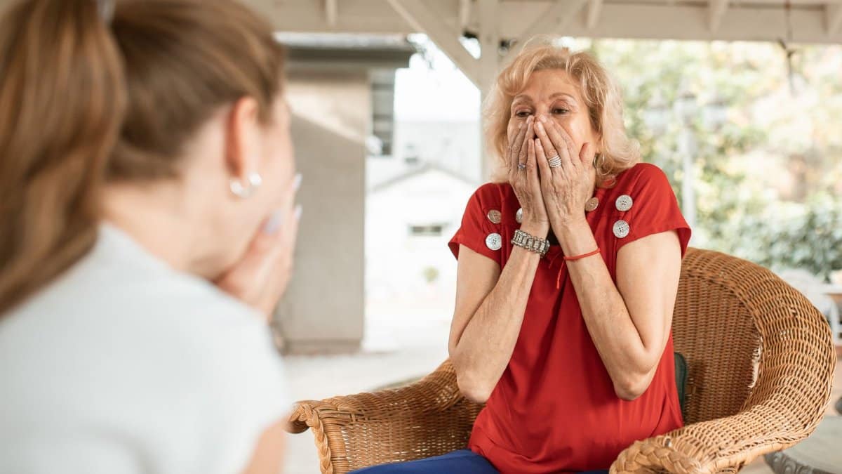An elderly woman expresses surprise and joy during an outdoor conversation.