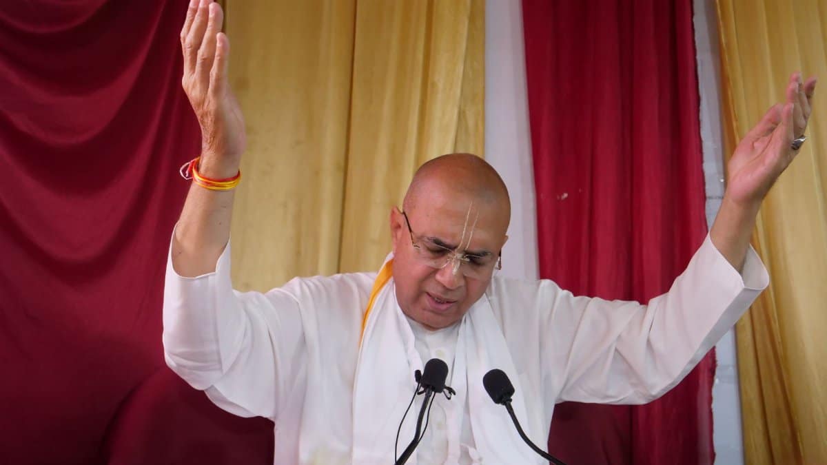 A religious figure in white clothing prays with raised arms during a spiritual gathering.