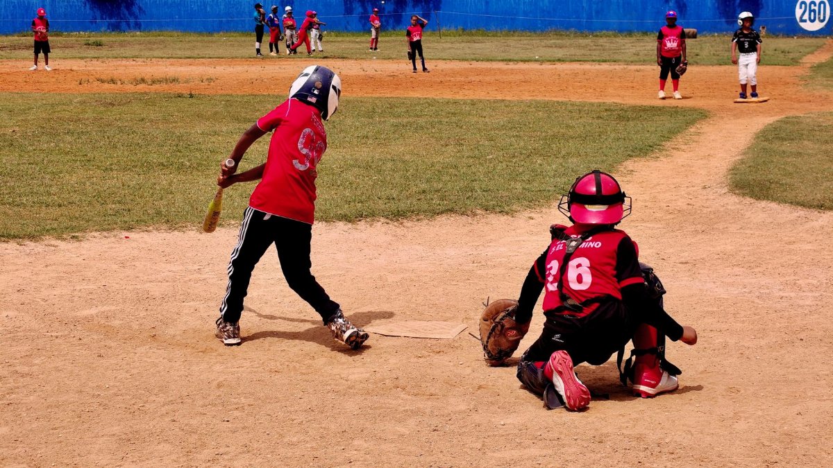 A youth baseball game in progress with kids playing on a sunny day, wearing protective gear.