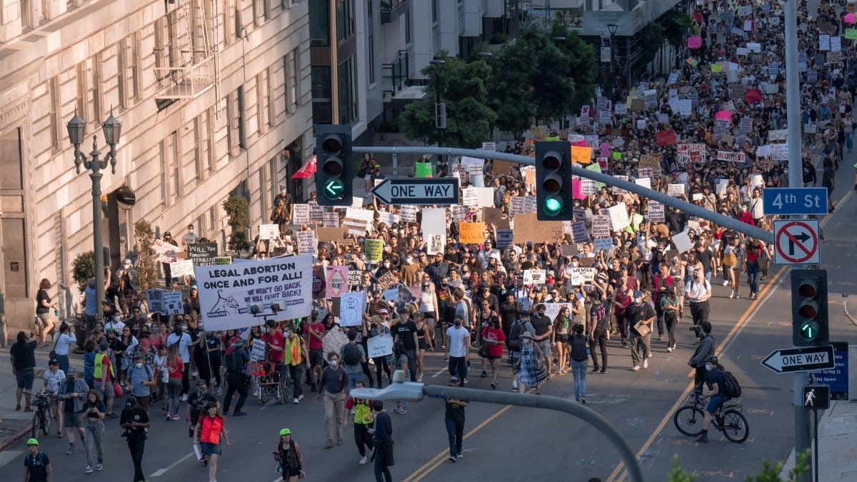 A diverse crowd in Los Angeles rallies for legal abortion rights, holding various placards on a city street.