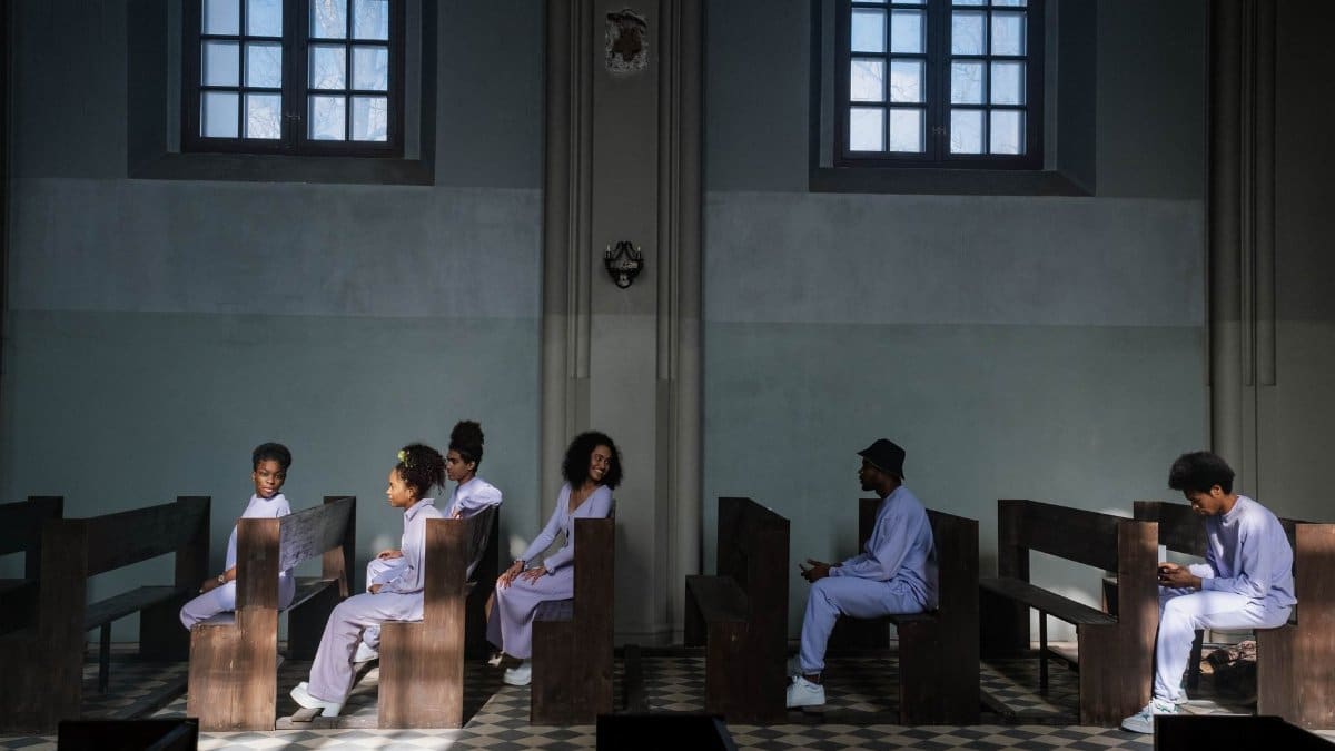 Group of choir members seated in church pews with soft daylight through windows creating a serene ambiance.