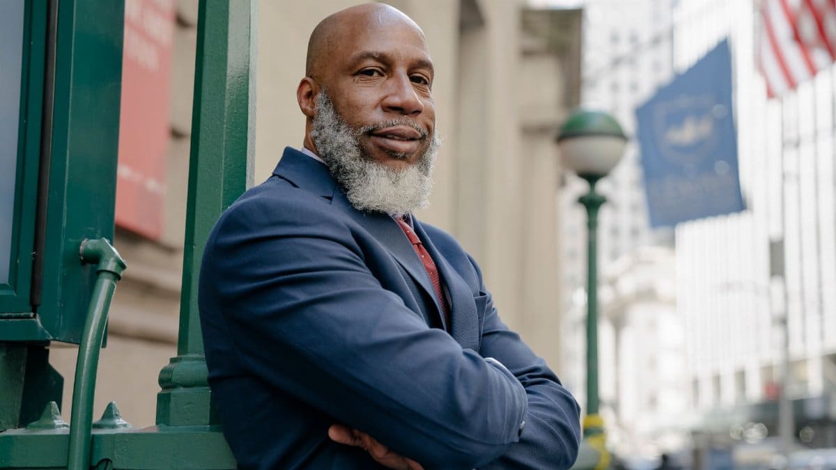 Confident man in a suit stands with arms crossed on a busy city street, exuding professionalism and determination.