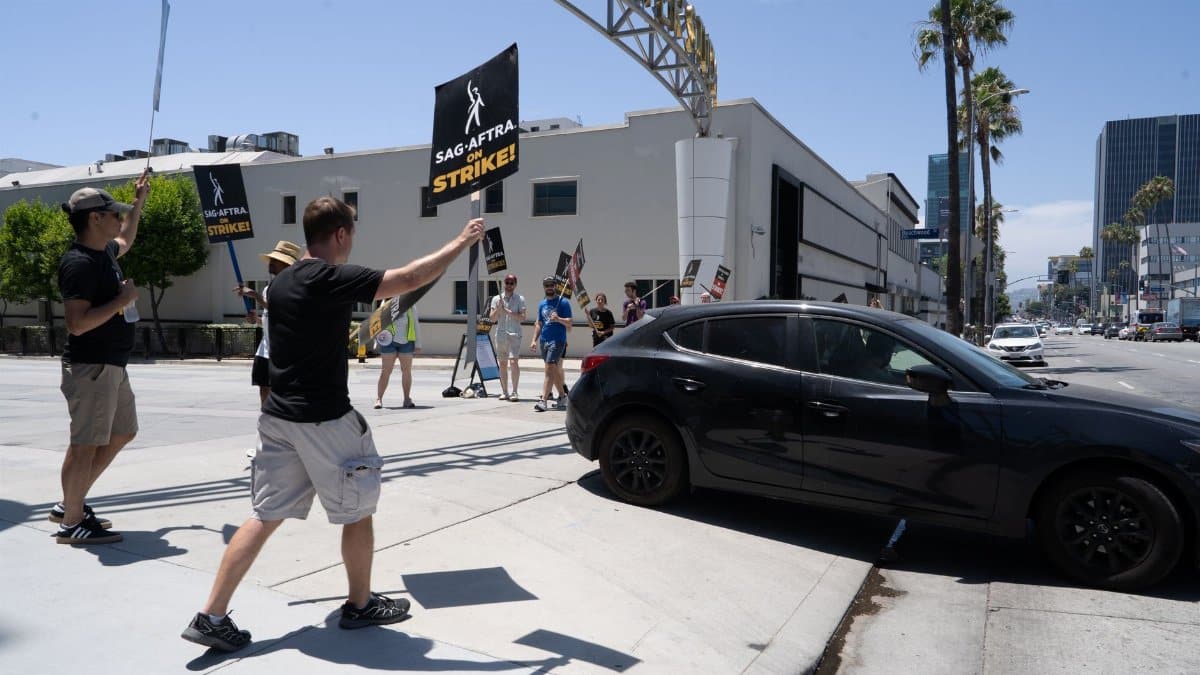 Participants in SAG-AFTRA strike wave signs and protest in a city setting.