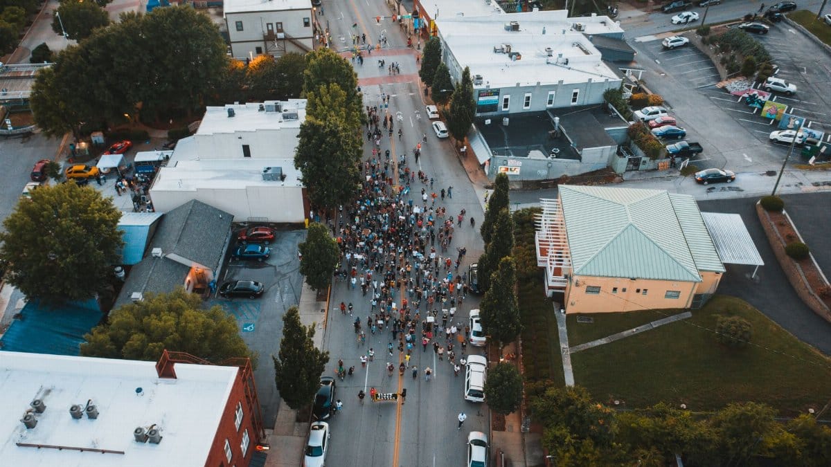 Aerial view of unrecognizable people on roadway between houses and trees during strike in town