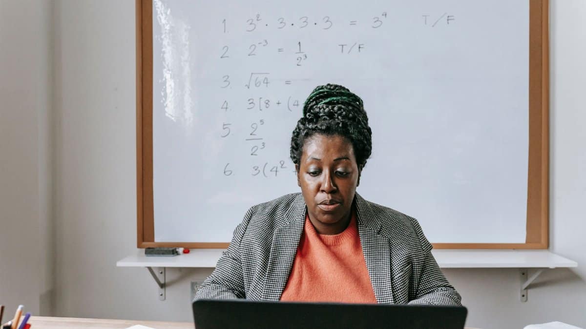 Pensive African American female explaining subject through internet on netbook in classroom with whiteboard