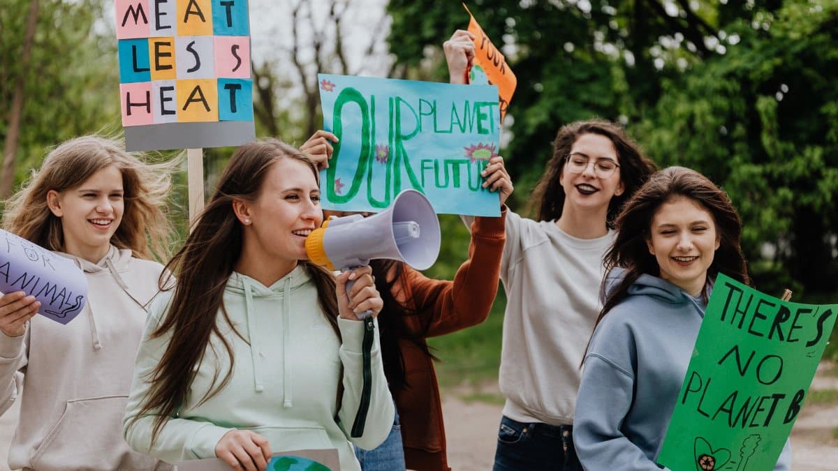 Group of young women at a climate protest holding signs with environmental messages outdoors.