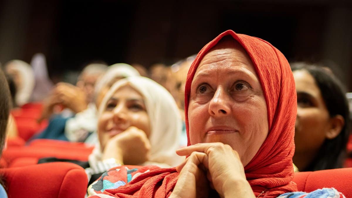 Diverse audience members attentively watching a speaker at a cultural event indoors.