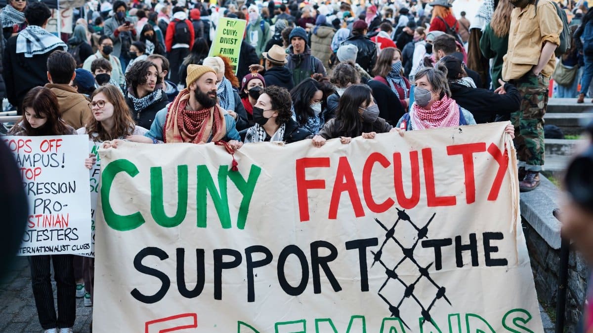 Crowd gathers for CUNY faculty support protest with signs and banners advocating demands.