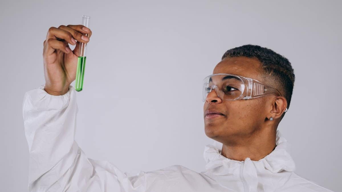 Young male scientist in protective gear examining a test tube in a laboratory setting.