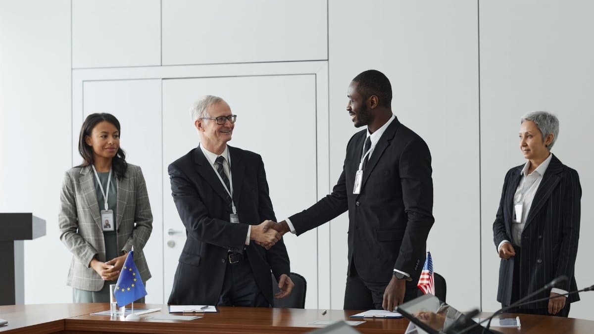 Business professionals shaking hands in conference room with flags signifying international agreement.