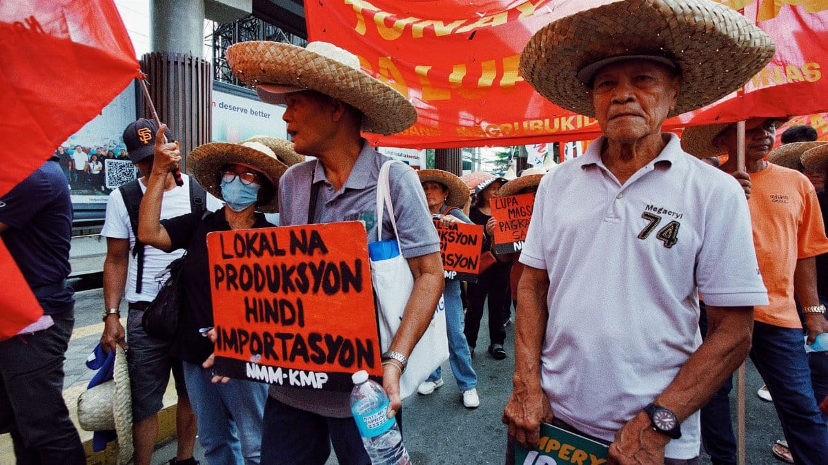 Farmers march advocating local production over importation. Wearing traditional hats, they hold colorful banners.