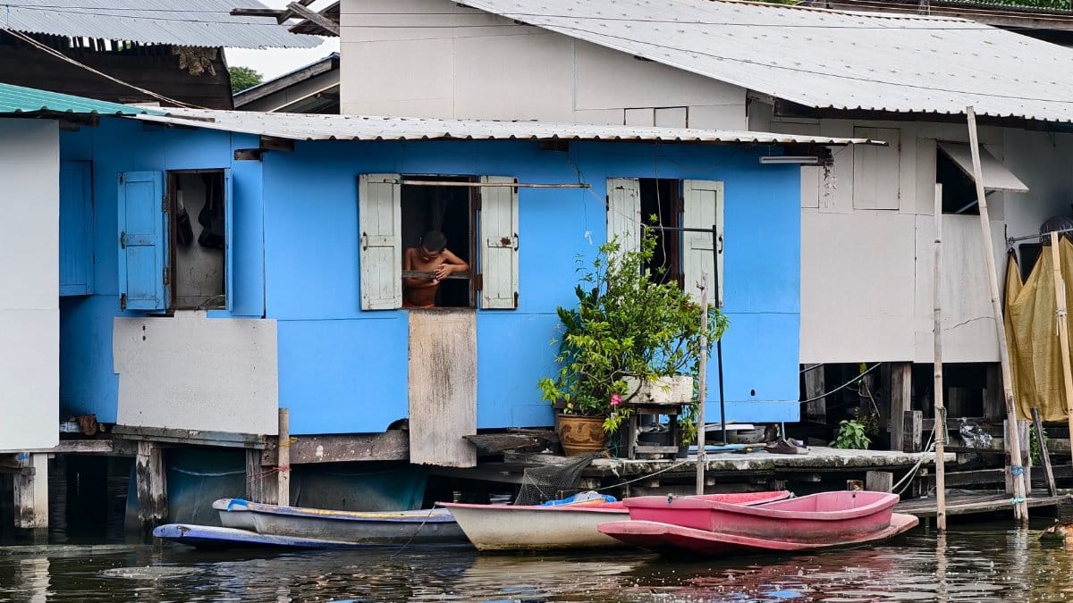 Quaint stilt house along a Bangkok canal with boats and a local resident visible.