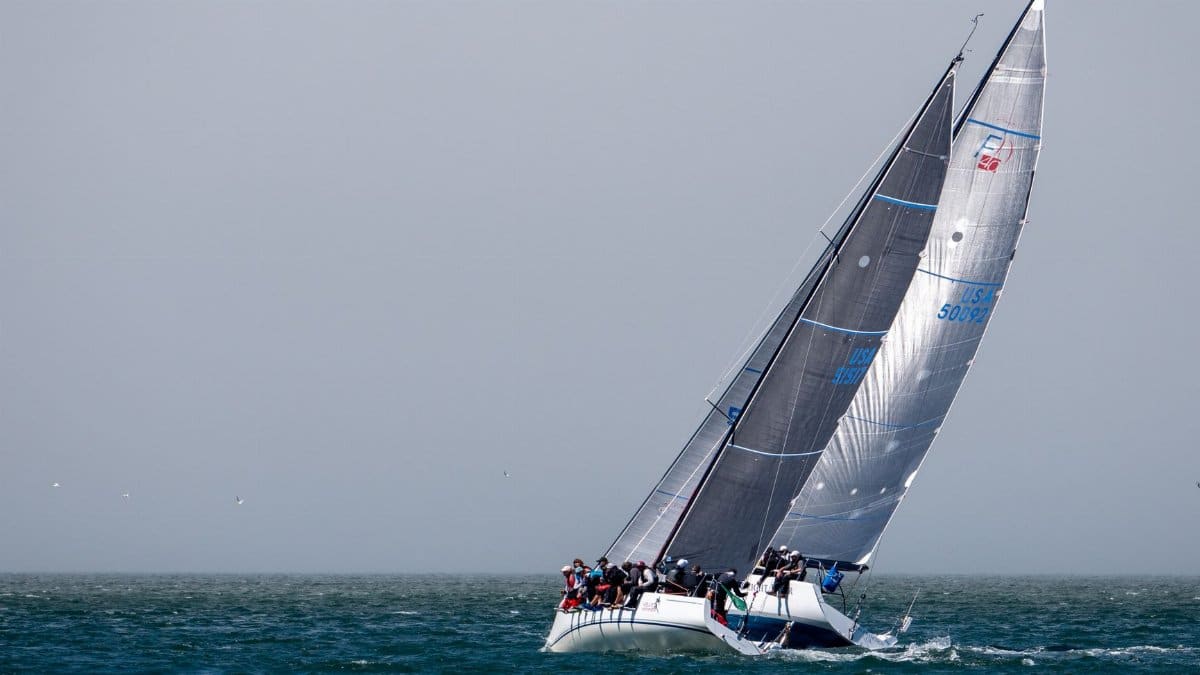 Dynamic sailing yacht with crew racing on open sea against gray sky.