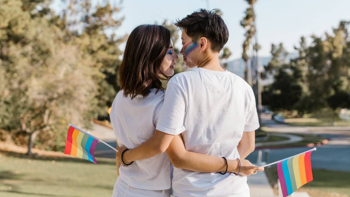 A loving couple embraces outdoors, holding rainbow flags, symbolizing LGBT pride and togetherness.