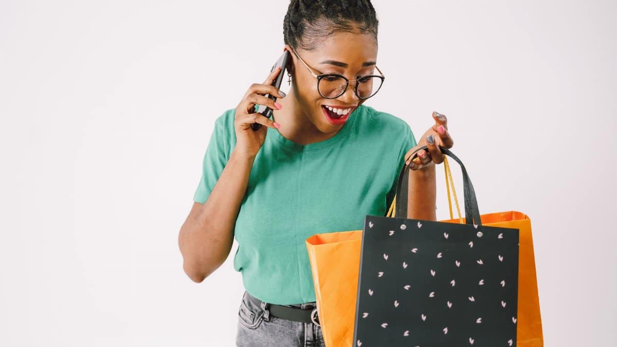 A cheerful woman holding shopping bags and chatting on her phone indoors.