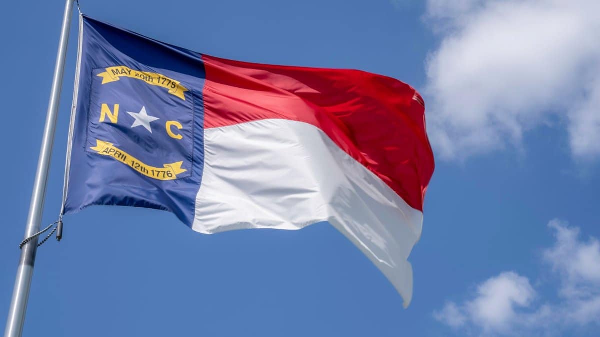 North Carolina state flag waving in the breeze with a clear blue sky backdrop.