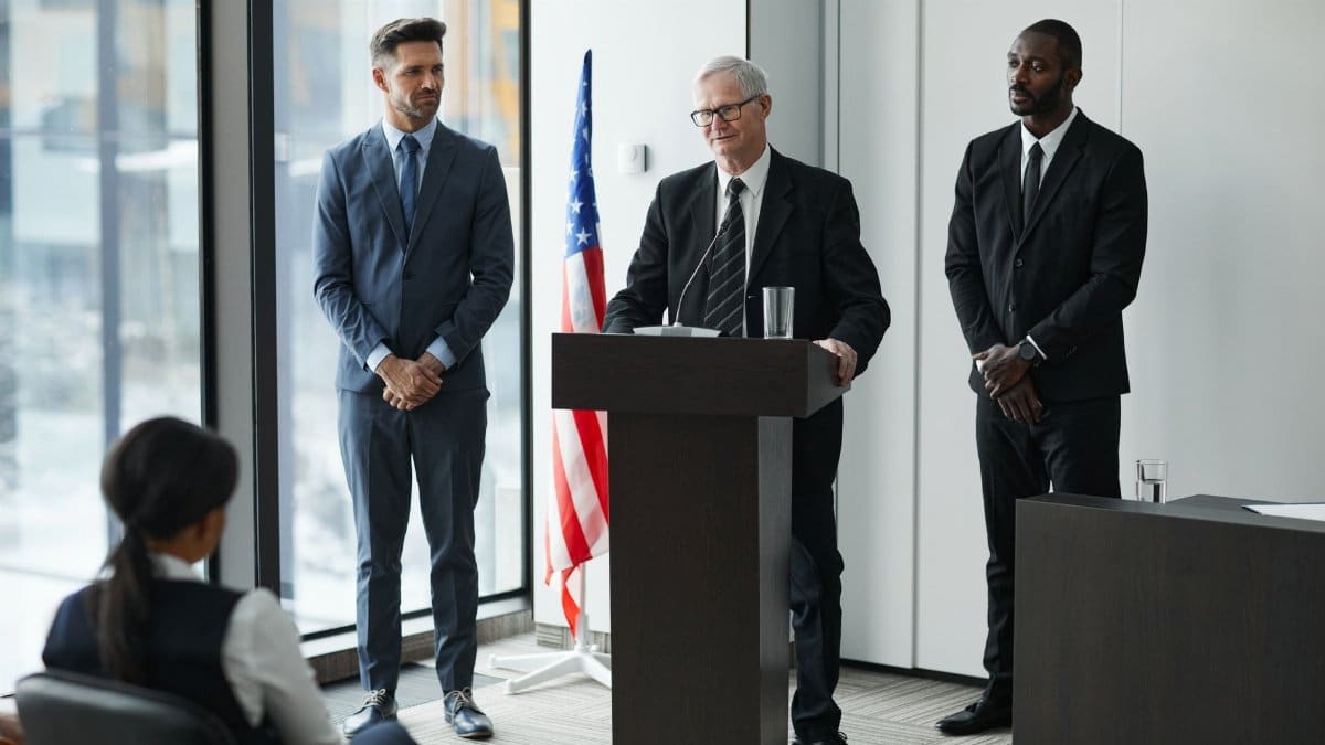 Officials delivering a political speech in a modern conference room with an American flag.