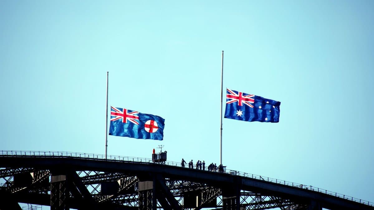 Australian and New South Wales flags flying on Sydney Harbour Bridge silhouette.