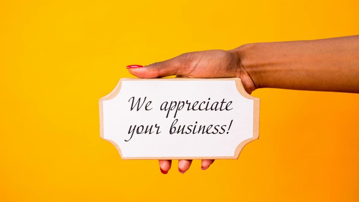 A hand holding a thank you sign with 'We appreciate your business!' on a vibrant yellow background.