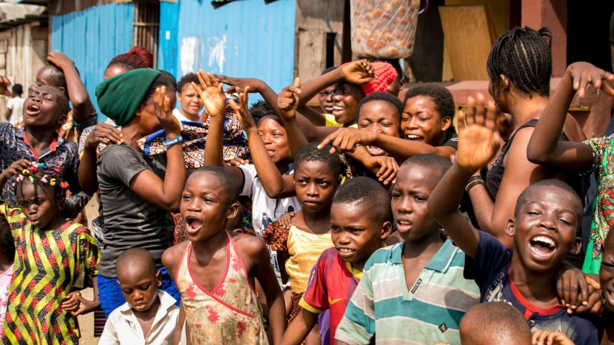 A diverse group of African children and adults celebrating at an outdoor community event.