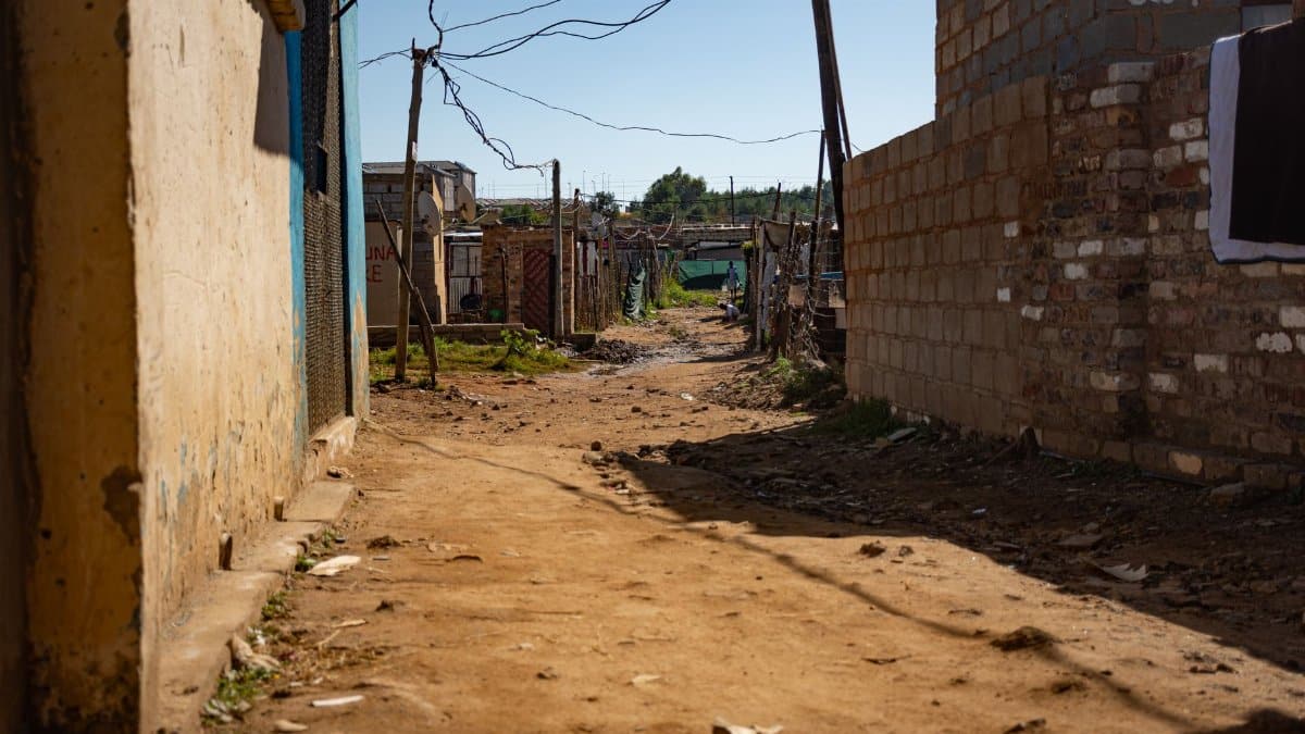 Dusty street lined with concrete walls in a Johannesburg township, under clear blue skies.