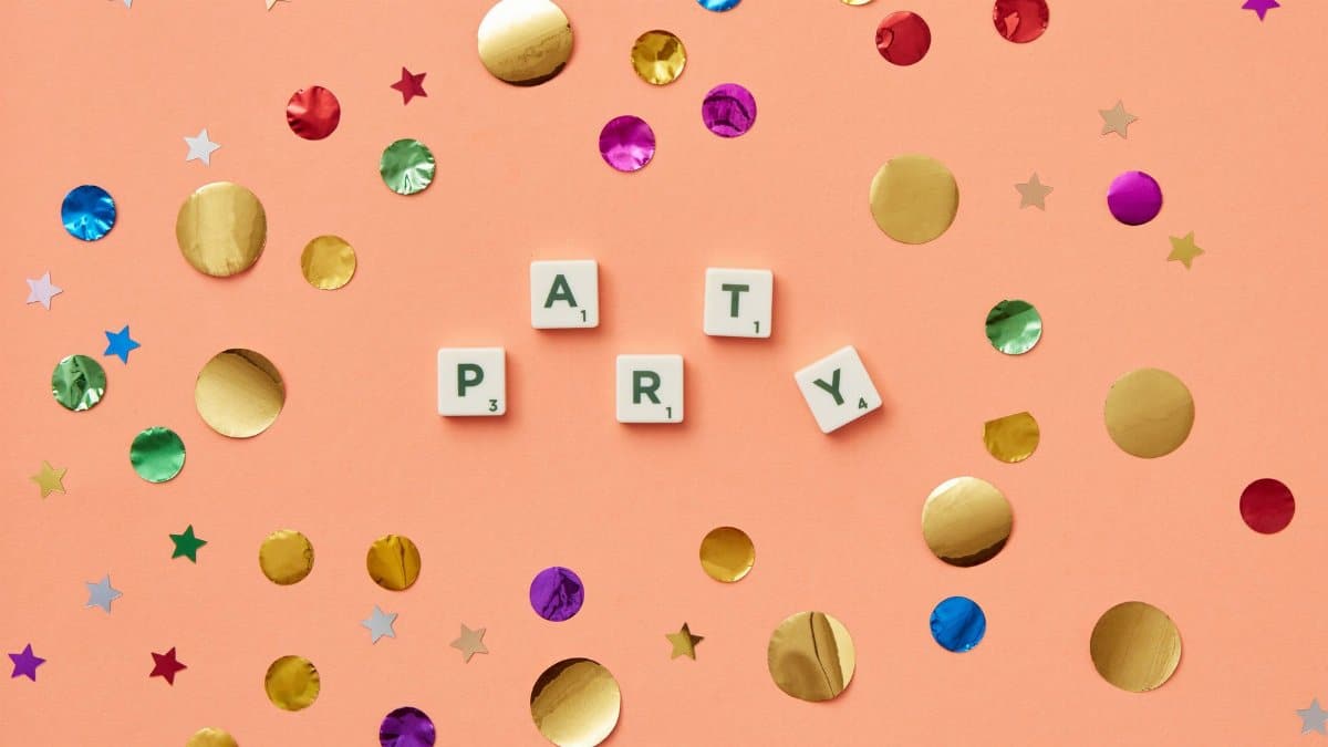 Party-themed Scrabble tiles spelling 'PARTY' surrounded by colorful confetti on a peach background.