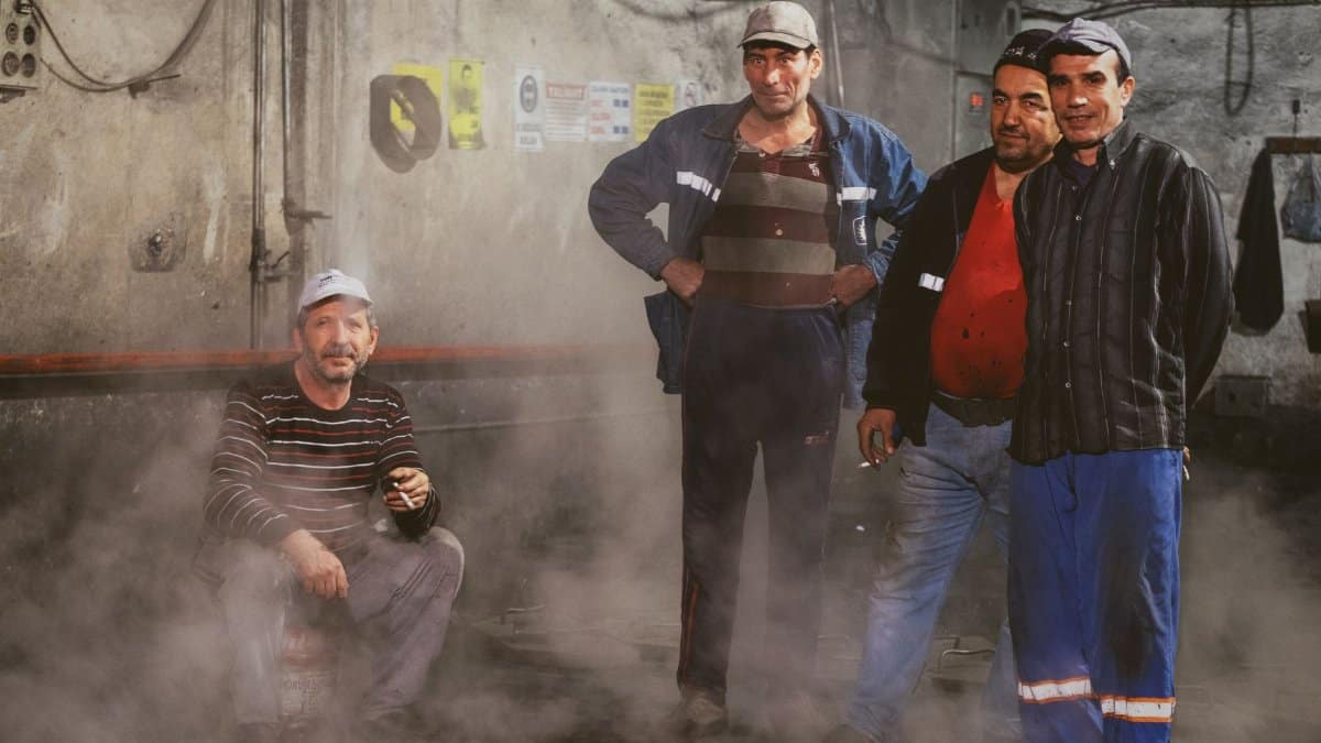 A group of industrial workers posing amidst machinery in a dimly lit factory setting.