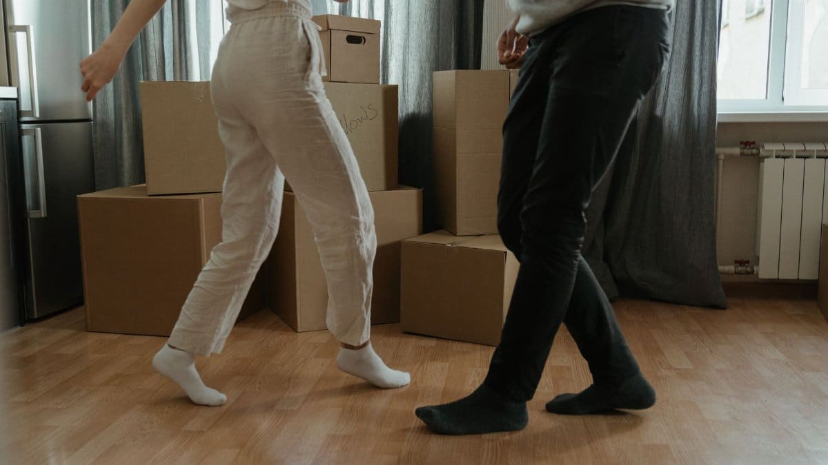 Two people dance joyfully amidst moving boxes in their new home.