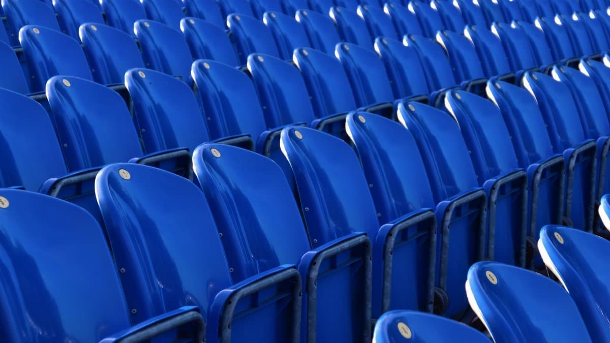 Rows of blue plastic seats in a vacant outdoor stadium on a sunny day.
