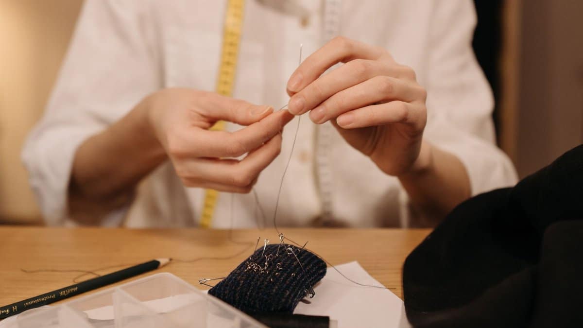 Detailed view of hands sewing fabric with needle and thread, capturing the art of tailoring.