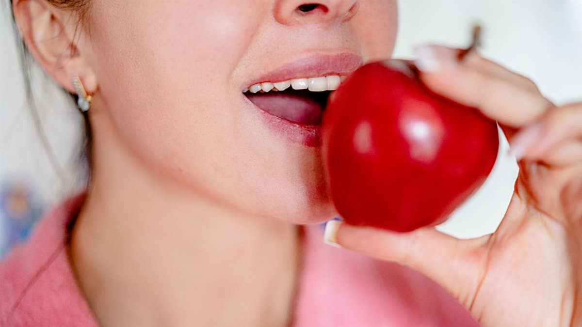 Close-up of a woman about to bite a red apple, showcasing healthy eating.