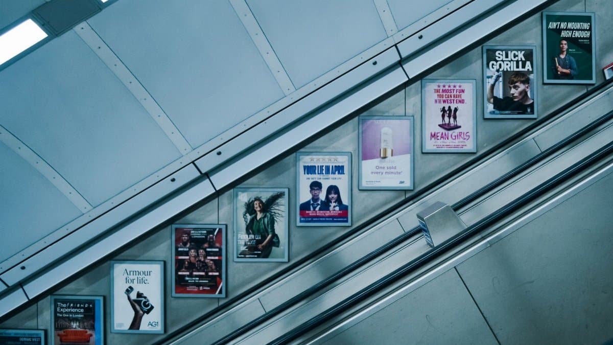 Vibrant posters along an escalator in the London Underground, showcasing various advertisements.
