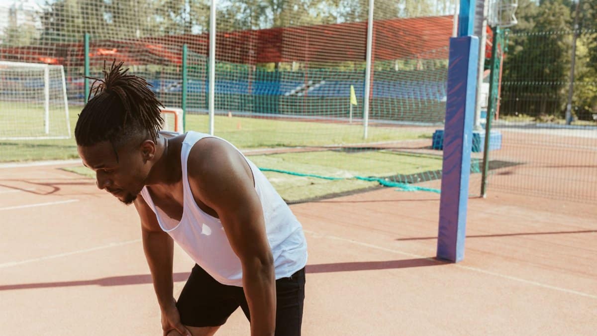 Tired athlete resting after exercise on a sunny outdoor sports field.