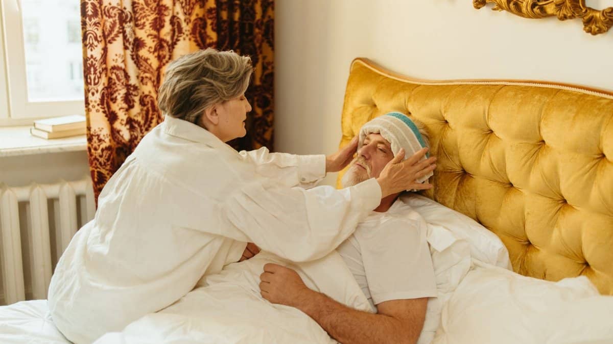 A woman provides care to an unwell man in bed, showing warmth and affection.