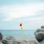 A red warning flag on a sandy beach in Oaxaca, Mexico, with ocean and rocky foreground.