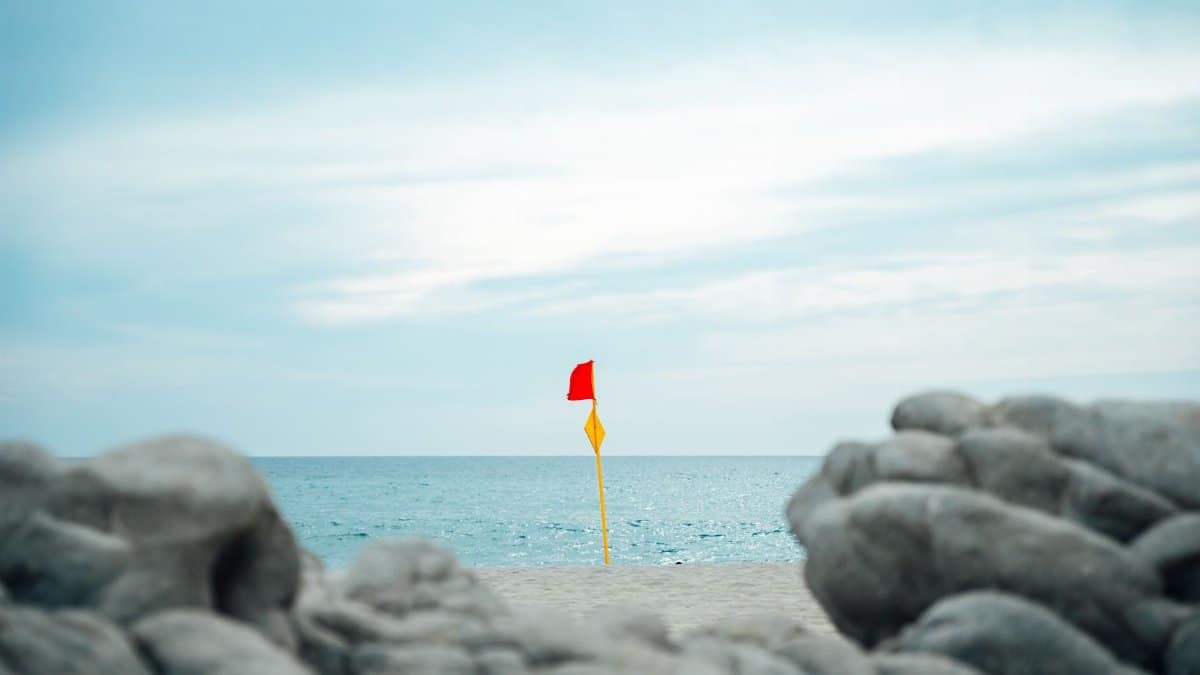 A red warning flag on a sandy beach in Oaxaca, Mexico, with ocean and rocky foreground.