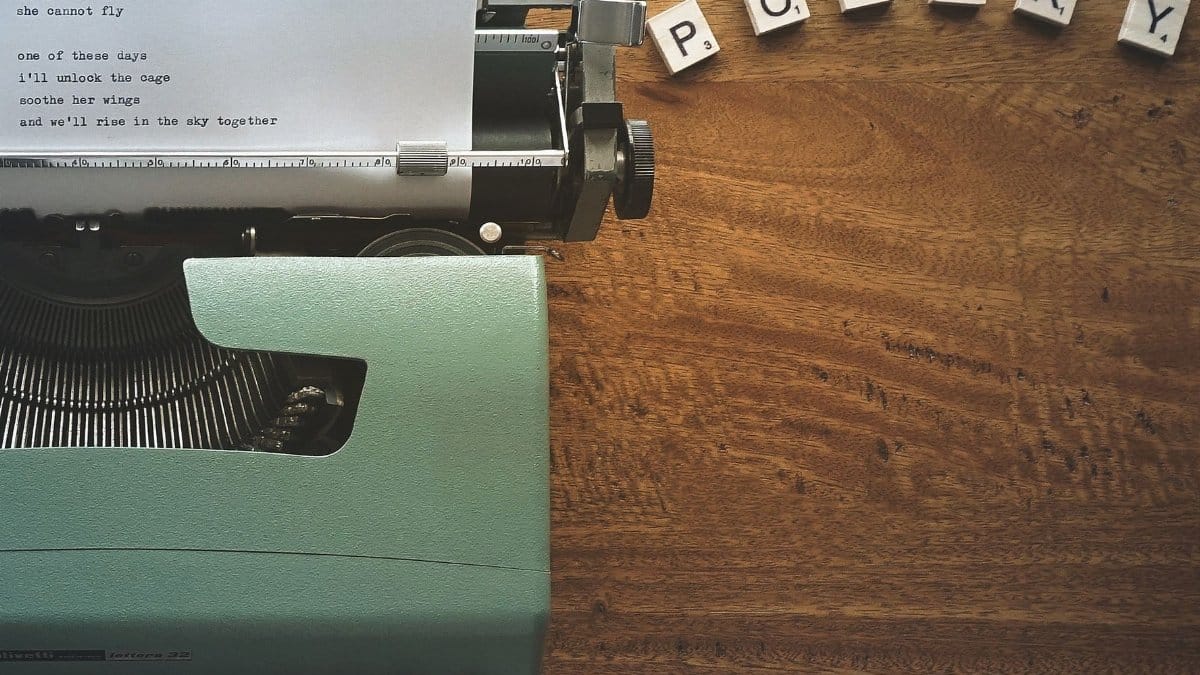 A typewriter creates poetic lines on paper amidst Scrabble tiles spelling 'POETRY'.