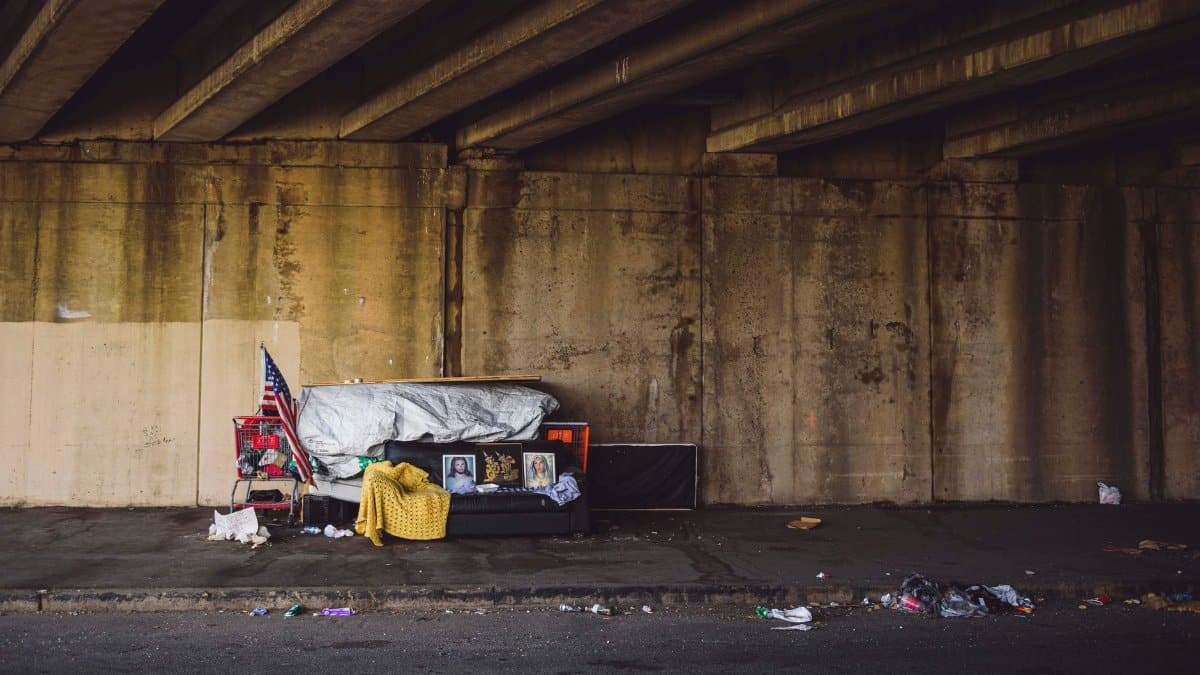 A gritty urban underpass in Philadelphia with signs of homelessness and American flag.