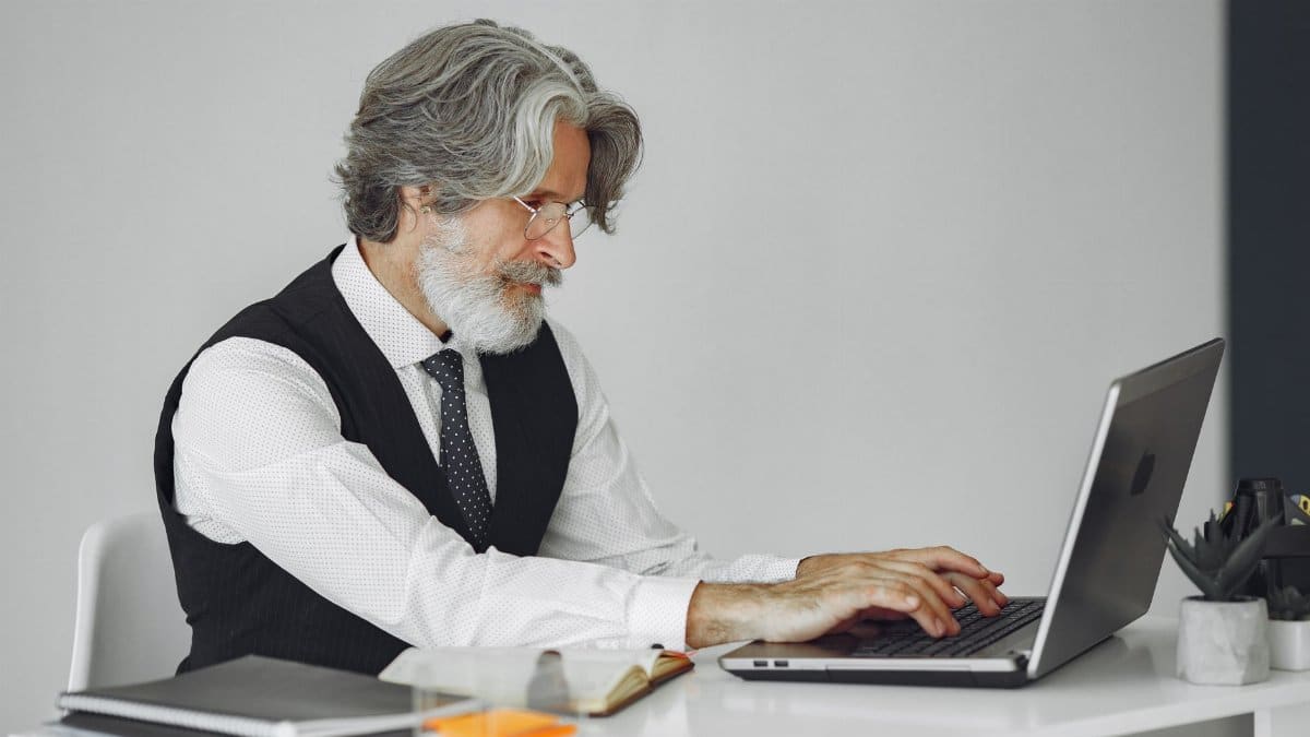 Elegant senior man in office attire typing on a laptop at a desk.