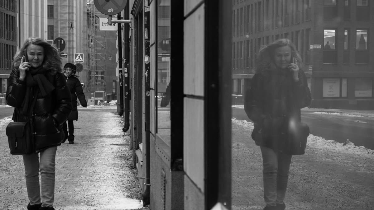 Black and white photo capturing urban street life with a focus on pedestrians and reflections.