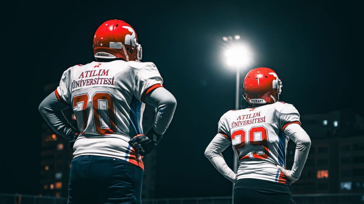Football players in Atılım University jerseys standing under stadium lights at night.