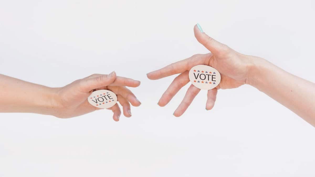 Two hands exchanging vote stickers symbolizing political participation and civic duty.